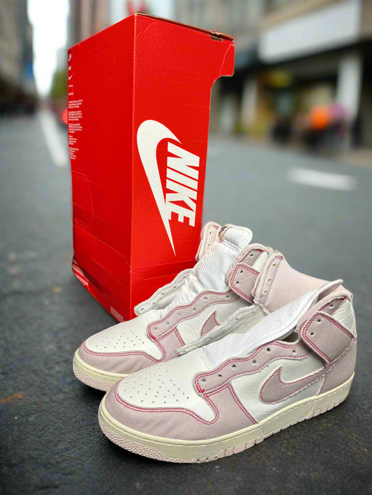 Pink sneakers with white soles next to a red Nike box on a dark surface